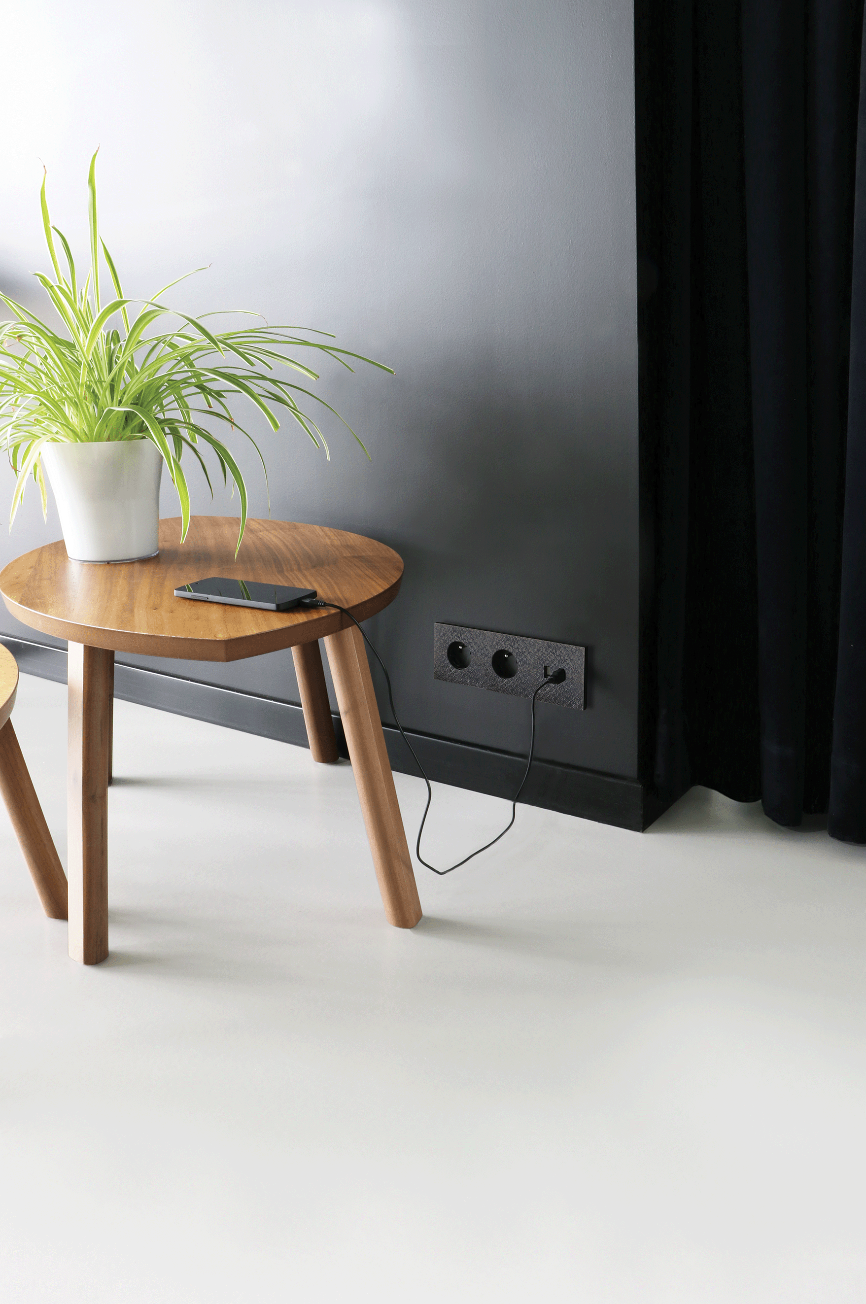 Basalte 2-fach Schuko-Steckdose im dunklen Designrahmen mit Ladekabel in modernem Wohnraum