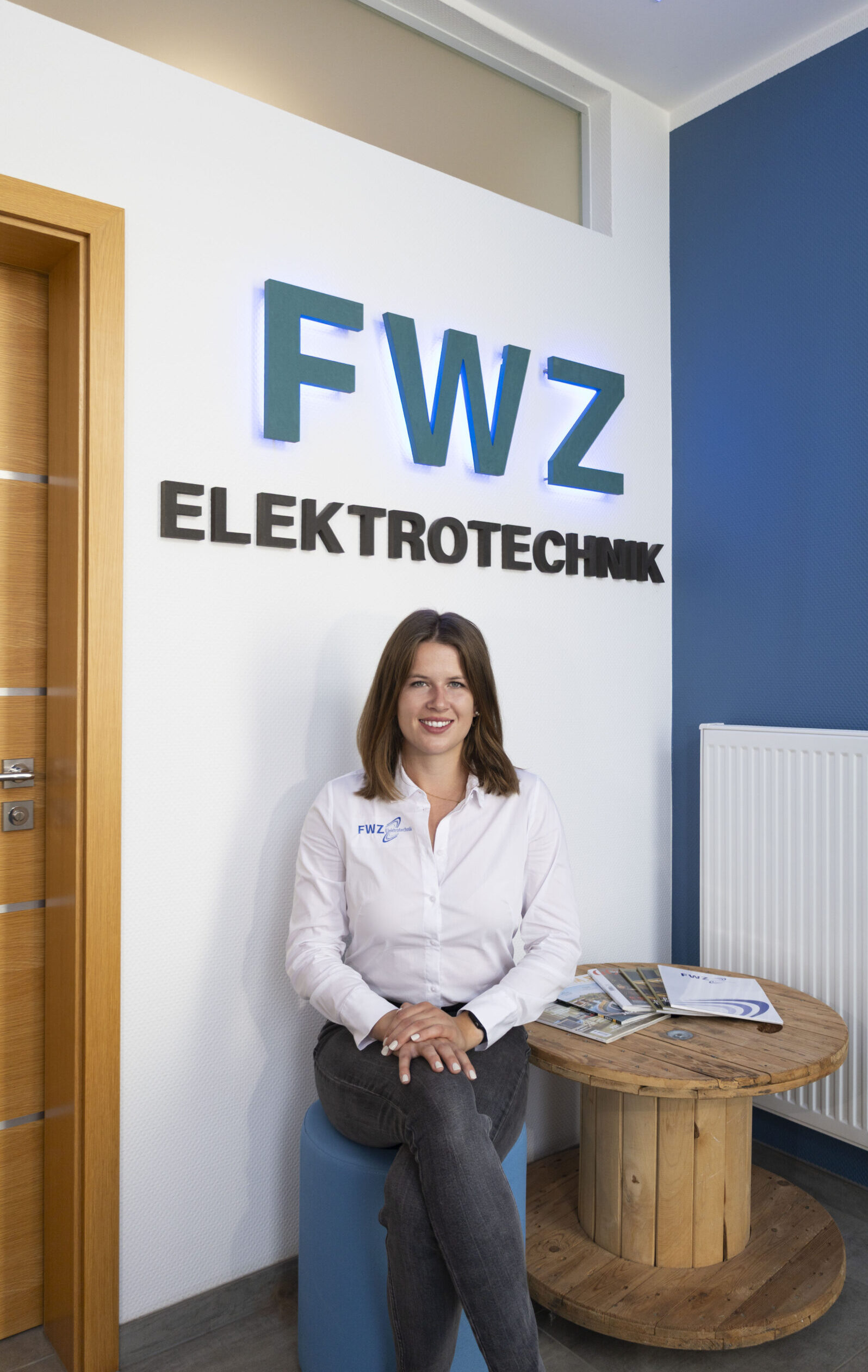 Aileen Richter von FWZ Elektrotechnik im Büro vor dem Firmenlogo.
