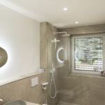 Modernes Badezimmer mit heller, neutralweißer Beleuchtung, Deckenstrahlern und offener Dusche.