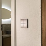 Basalte Sentido KNX-Taster aus gebürstetem Metall an weißer Putzwand – FWZ Elektrotechnik Smart Home Referenz.