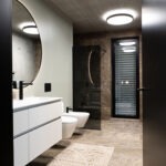 Moderne Badezimmerbeleuchtung mit runden Deckenleuchten und hinterleuchtetem Spiegel – FWZ Elektrotechnik Referenz Villa am Main.