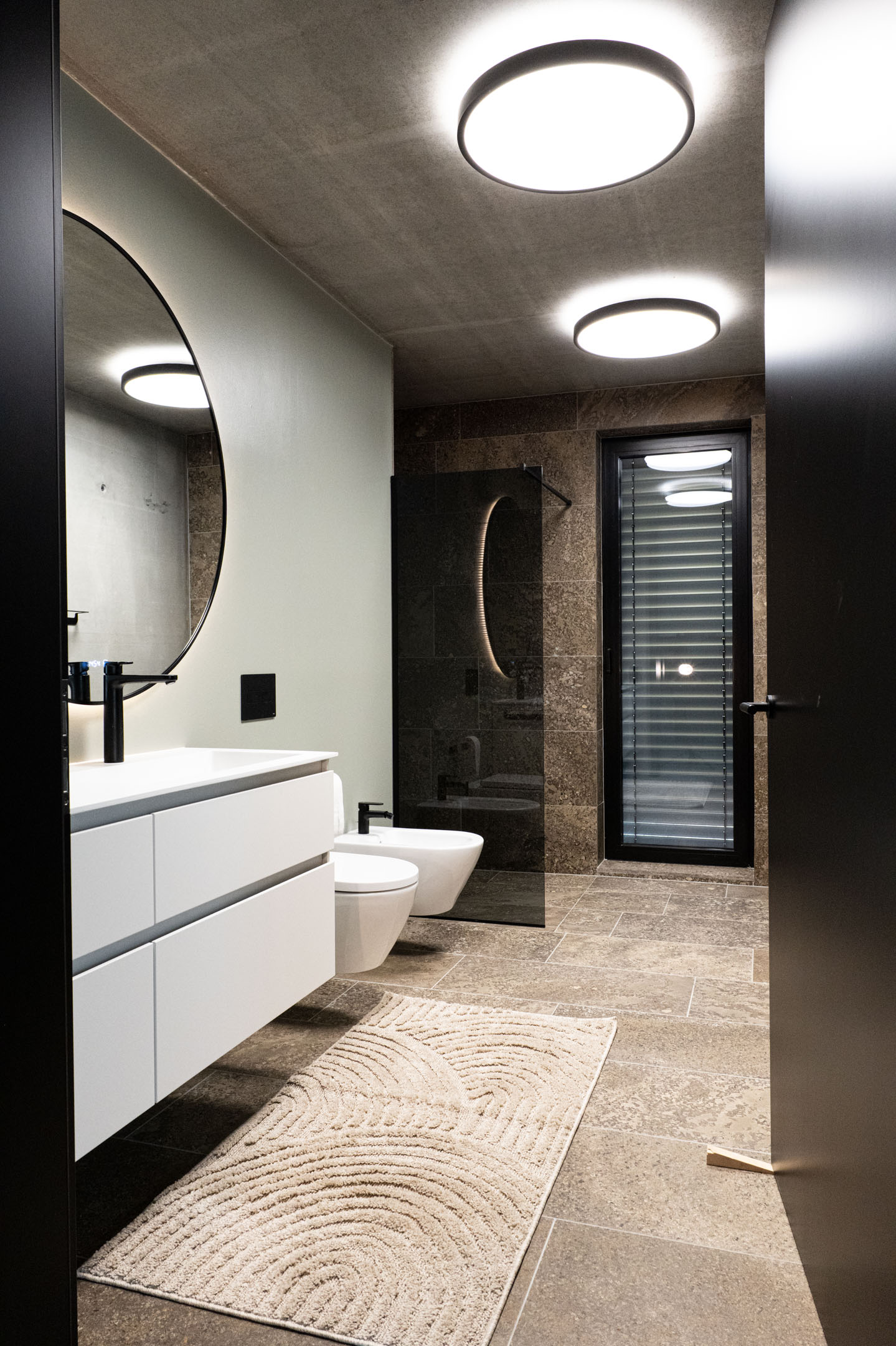 Moderne Badezimmerbeleuchtung mit runden Deckenleuchten und hinterleuchtetem Spiegel – FWZ Elektrotechnik Referenz Villa am Main.