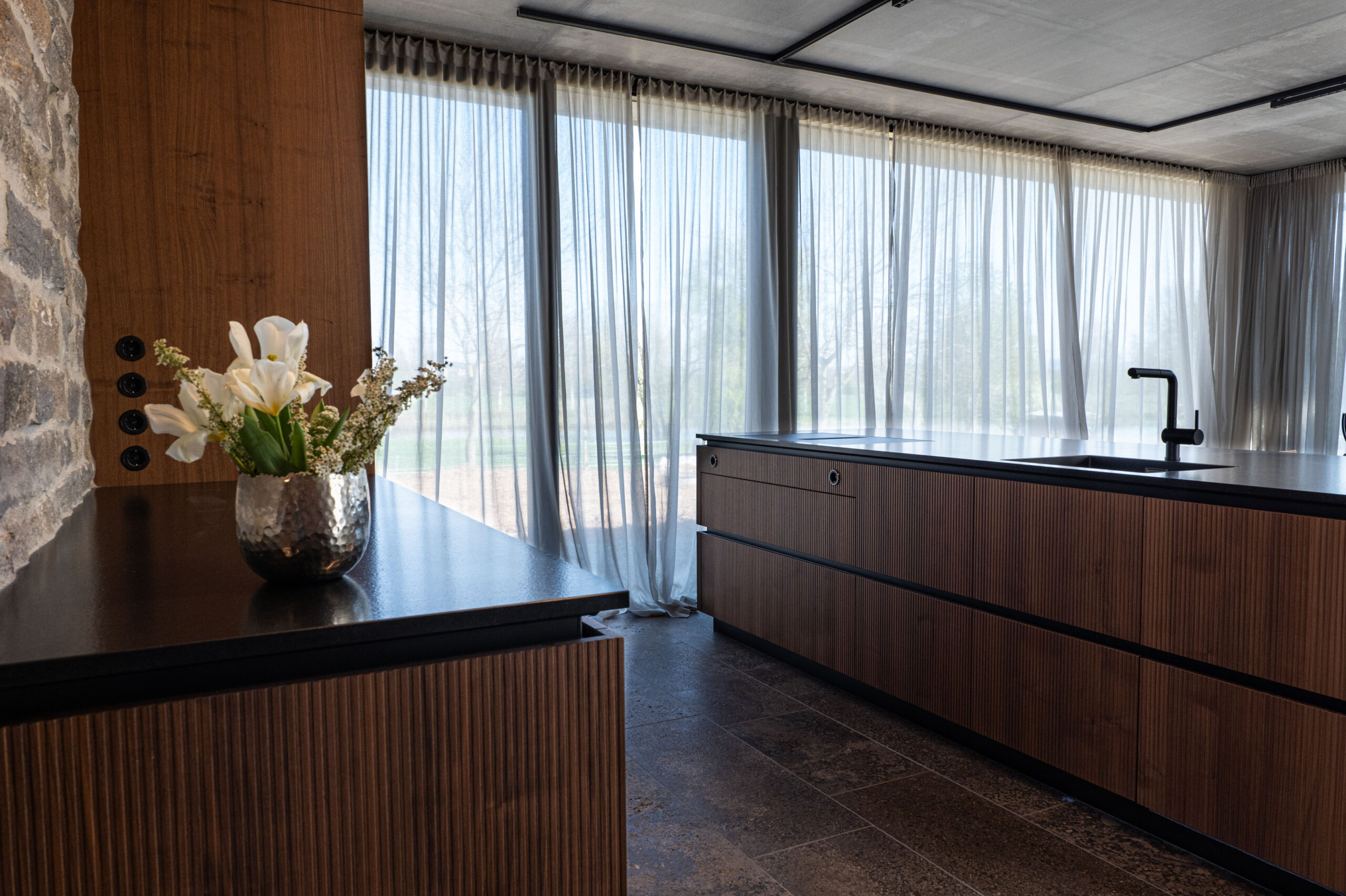 Schwarze Steckdosenleiste bündig integriert in Holzpaneel einer Luxusküche – FWZ Elektrotechnik Detail Villa am Main.