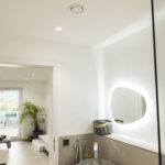 Modernes Badezimmer mit tageslichtweißer HCL-Beleuchtung, Deckenstrahlern und beleuchtetem Spiegel.