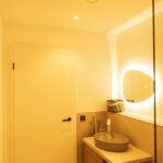 Modernes Badezimmer mit warmweißer HCL-Beleuchtung, Deckenstrahlern und beleuchtetem Spiegel in entspannter Abendszene.