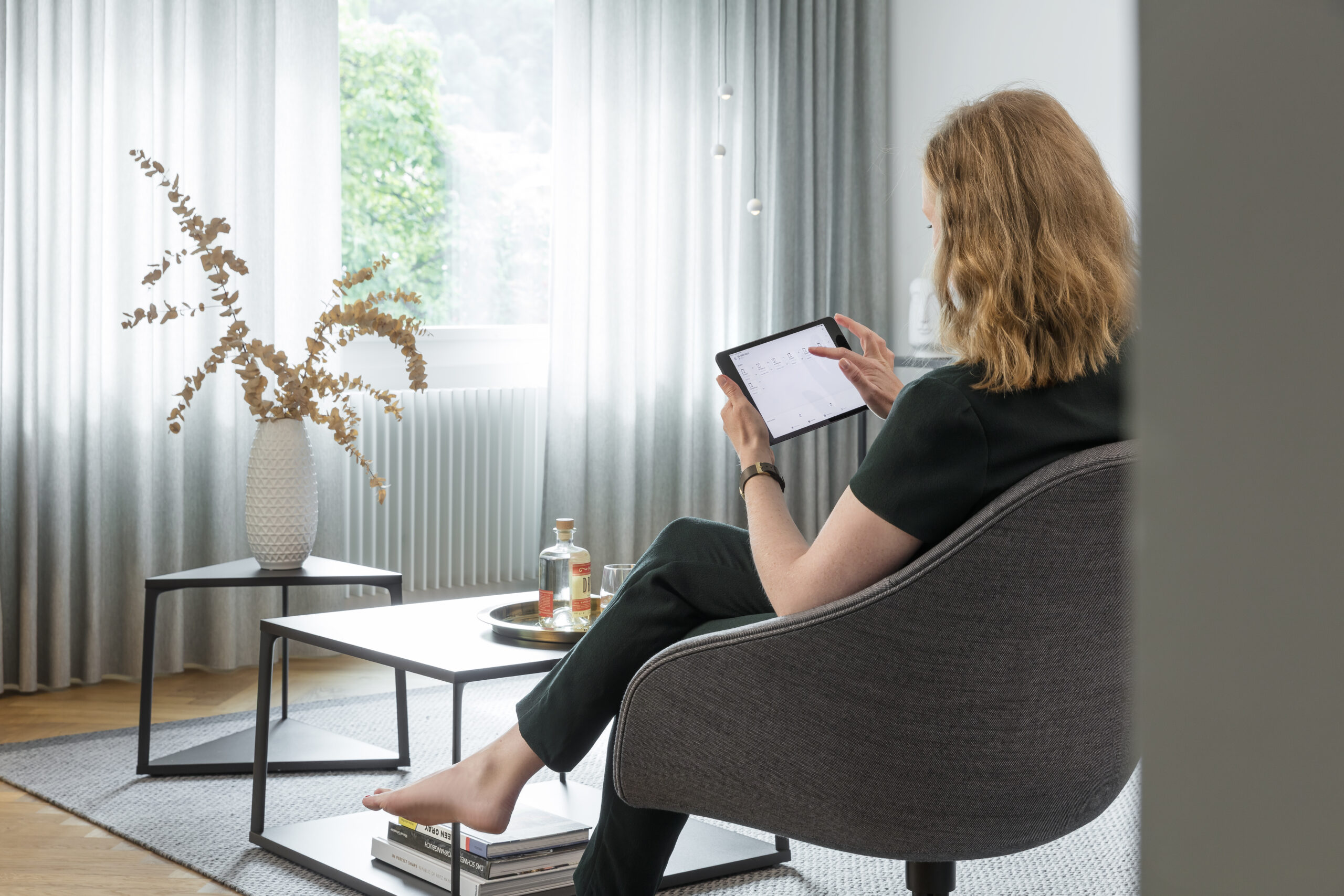 Wohnraum mit deckenhohen Vorhängen und Tablet-Steuerung für smarte Beschattung und Wohnkomfort.